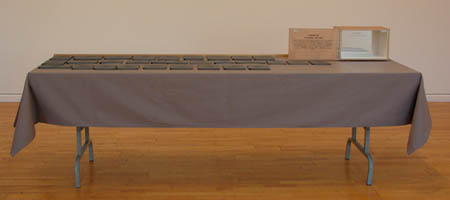 image, table recouverte d'une nappe grise servant à présenter des livres fantômes. A l'extrémité droite se trouve une boîte destinée au rangement des fantômes.